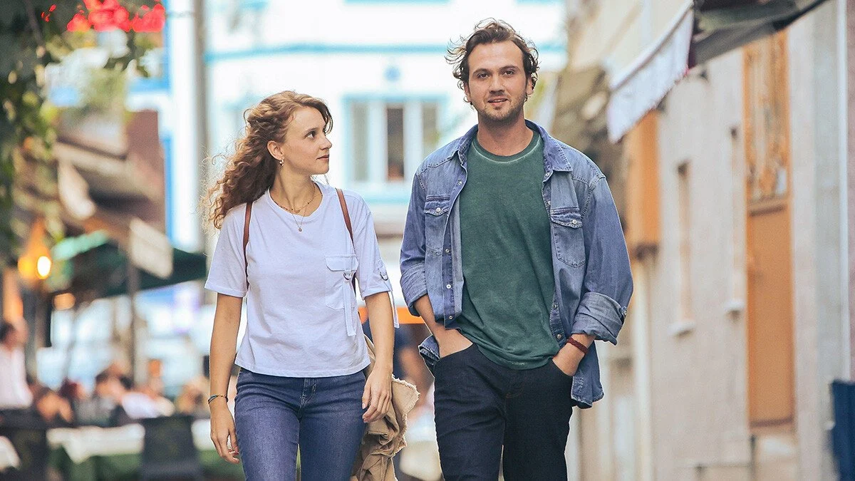 Devran caminha por uma rua ao lado de uma personagem em imagem promocional da série turca Deha