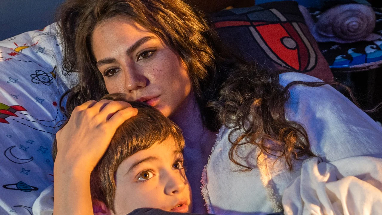 Farah abraça o filho Kerimşah enquanto os dois estão deitados, em cena da novela Meu Nome é Farah