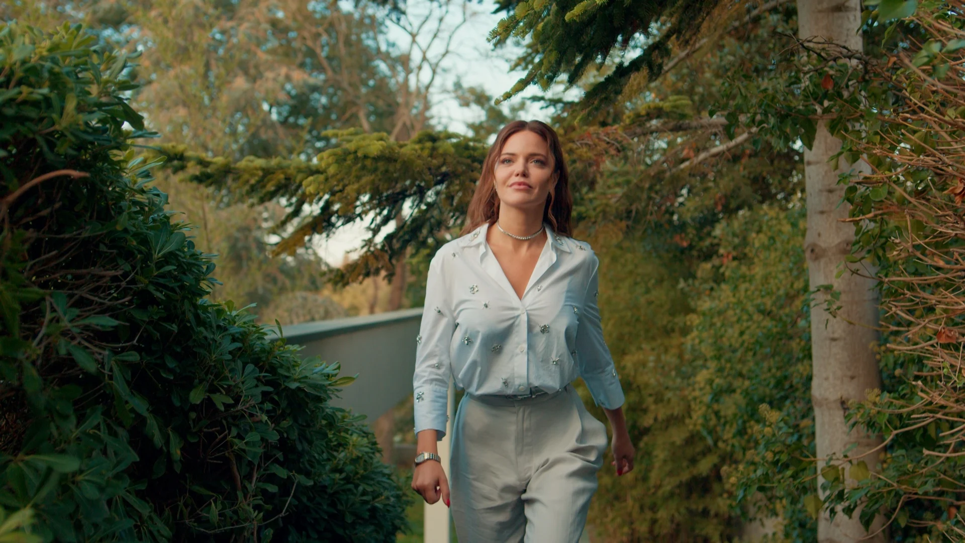 Sebnem vivida por Hilal Altınbilek caminha em um jardim na novela Minha Vida Perfeita