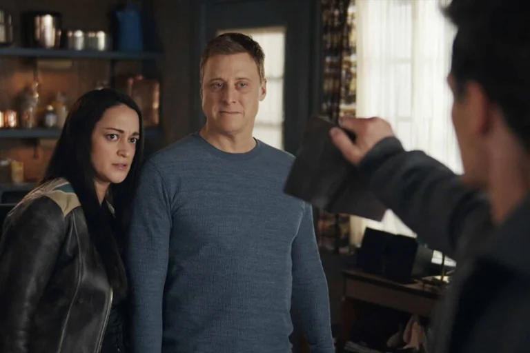 Asta e Harry olham para um homem que segura um livro em Resident Alien.