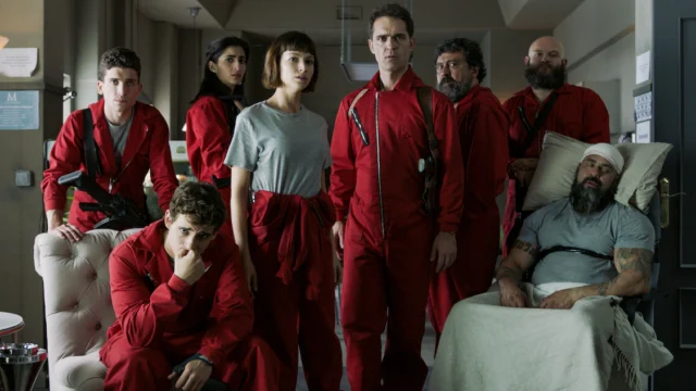 Integrantes do grupo de La Casa de Papel reunidos em uma sala, vários com macacões vermelhos.