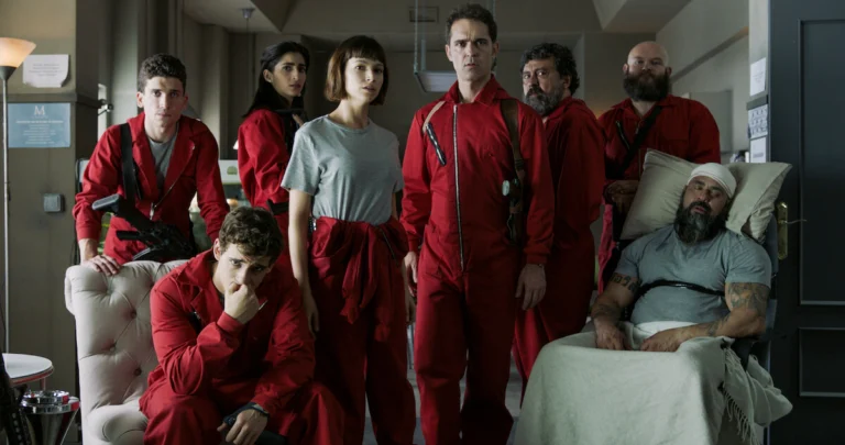 Integrantes do grupo de La Casa de Papel reunidos em uma sala, vários com macacões vermelhos.