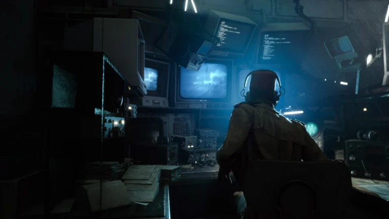 Combatente observa uma transmissão em um monitor, em uma sala escura iluminada por telas azuis.