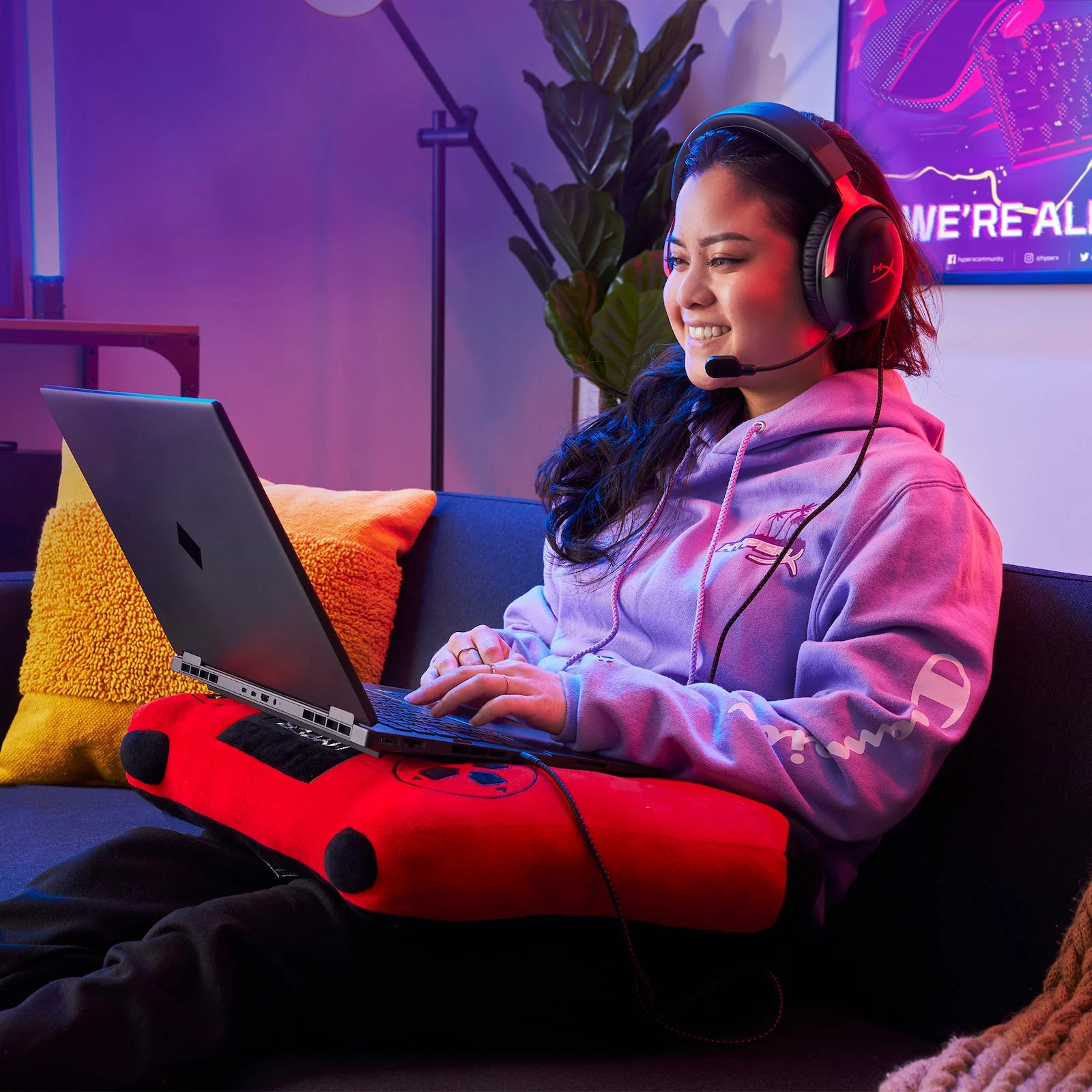 Pessoa usa um HyperX Cloud III com fio preto e vermelho enquanto joga em um notebook no sofá.