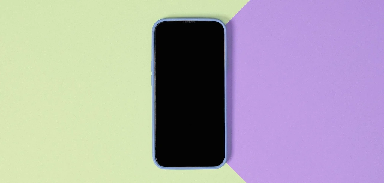 Celular com a tela apagada sobre uma superfície verde e roxa