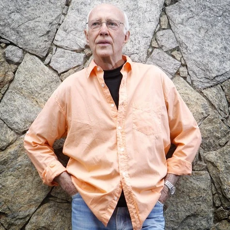 Roberto Maya de óculos e camisa clara fotografado em 2015 diante de uma parede de pedras