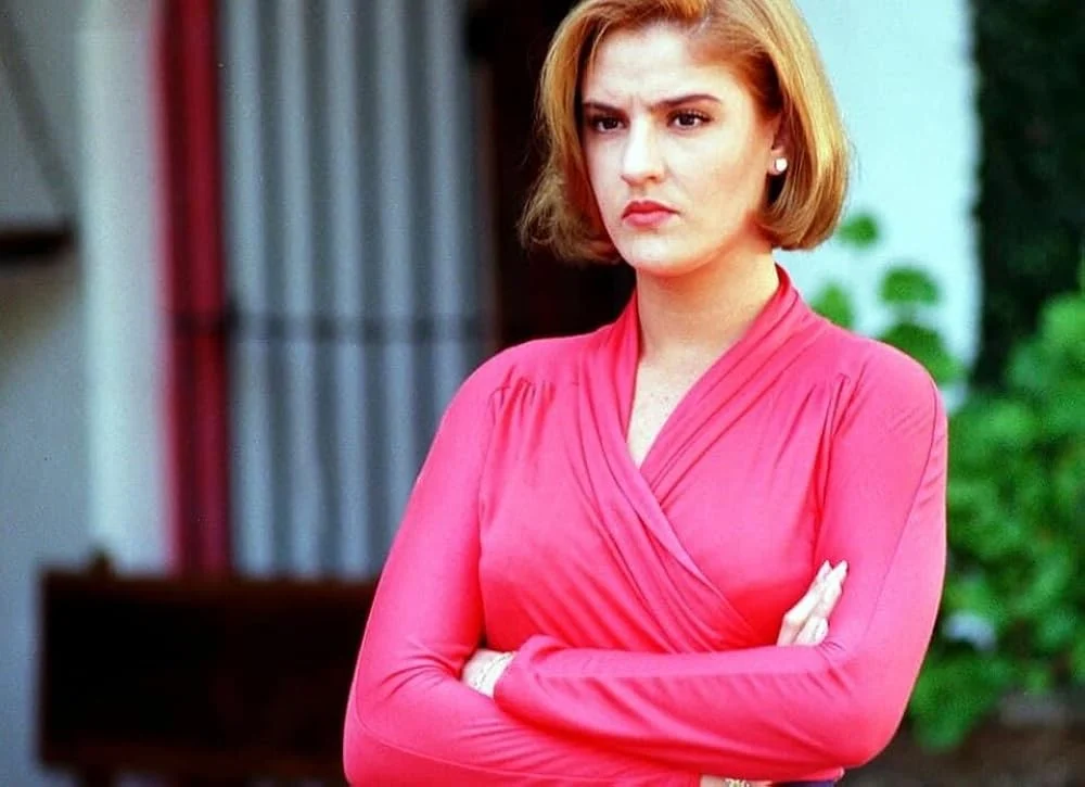 Chantal Andere como Angélica Santibáñez, usando blusa rosa e olhando com expressão séria