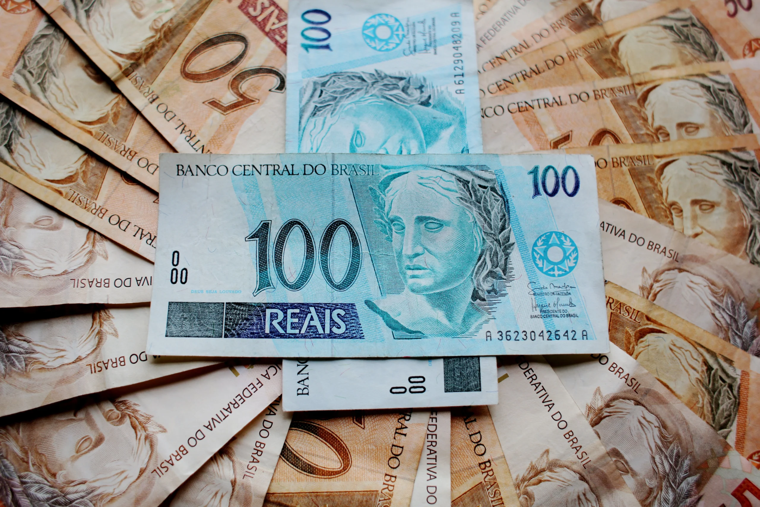Notas brasileiras de cinquenta e cem reais espalhadas, usadas para ilustrar o poder de compra da moeda brasileira