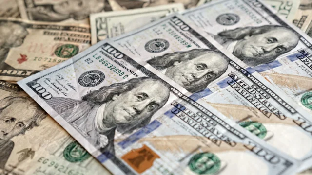 Notas de cem dólares espalhadas sobre uma superfície, em fotografia ilustrativa da cotação do dólar