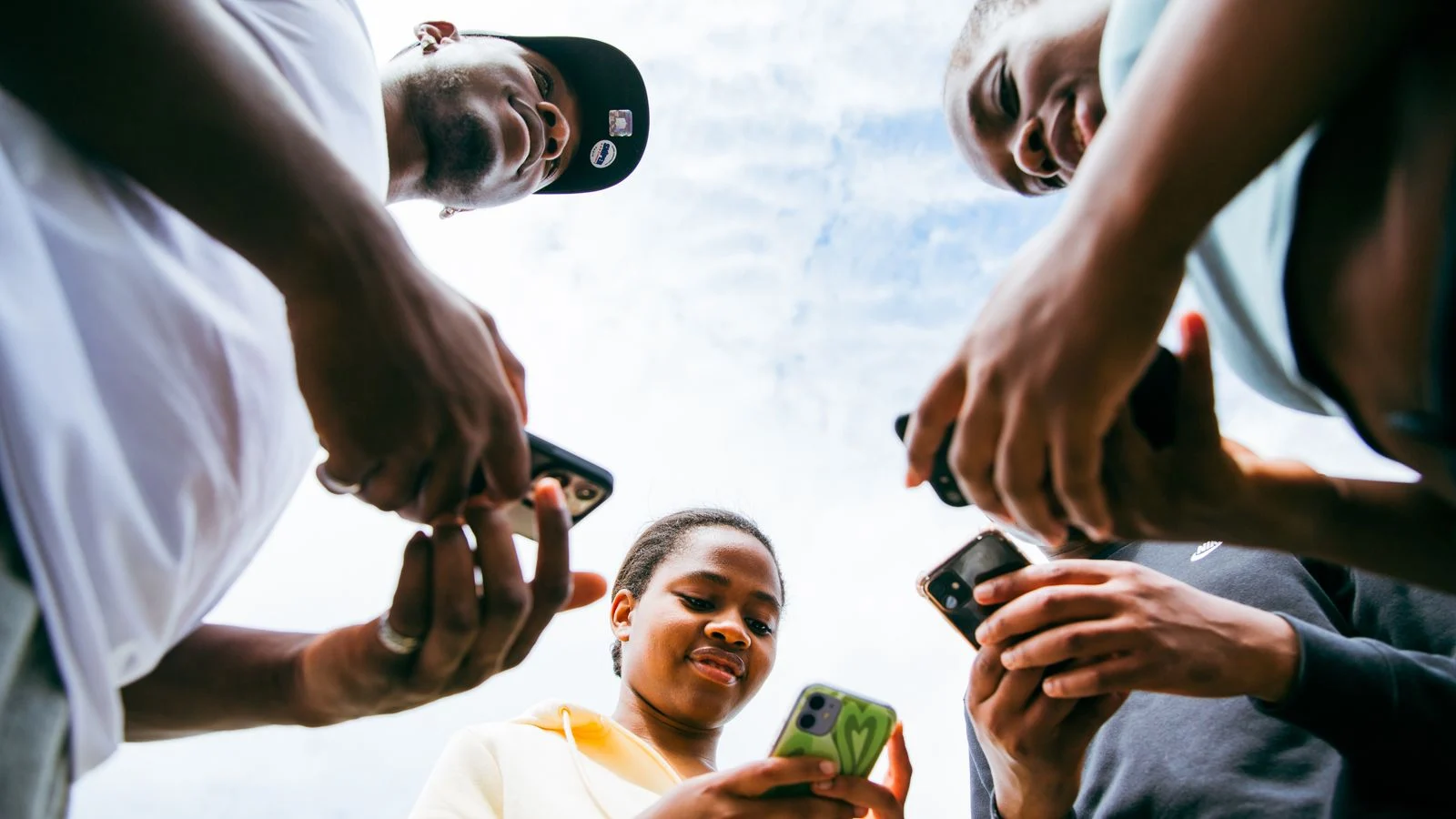 Grupo de pessoas reunidas ao ar livre usando celulares, representando conexões e comunidades digitais