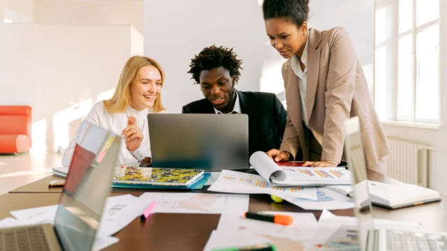 Profissionais reunidos em uma mesa de escritório observam a tela de um notebook