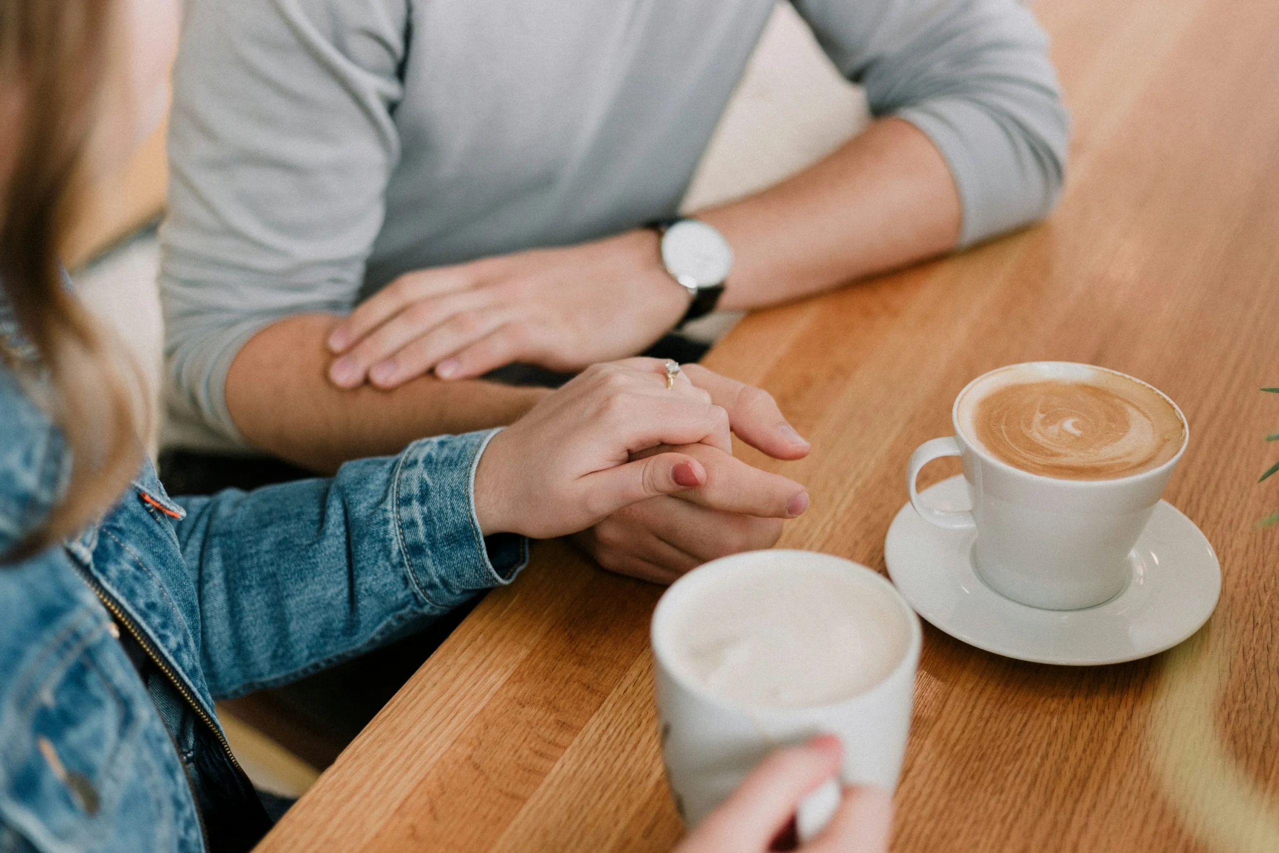 Duas pessoas de mãos dadas sobre mesa de cafeteria, representando encontro presencial com consentimento