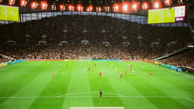 Campo de futebol visto da arquibancada de um estádio com torcedores