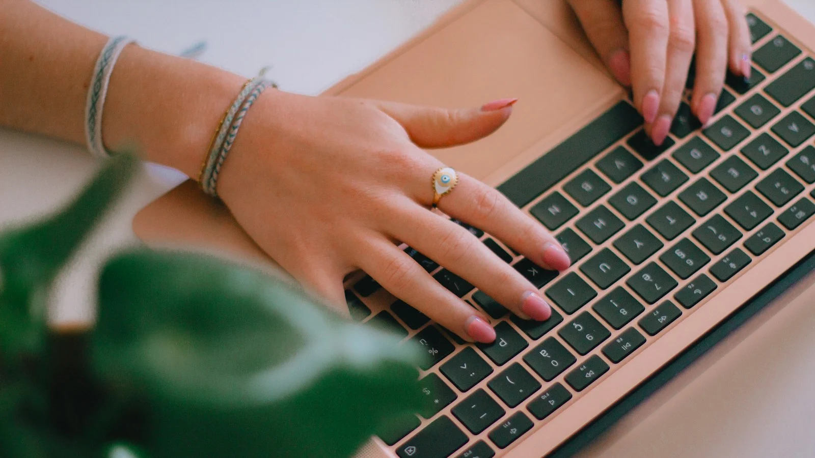 Pessoa digitando em notebook em uma mesa de trabalho com planta ao lado