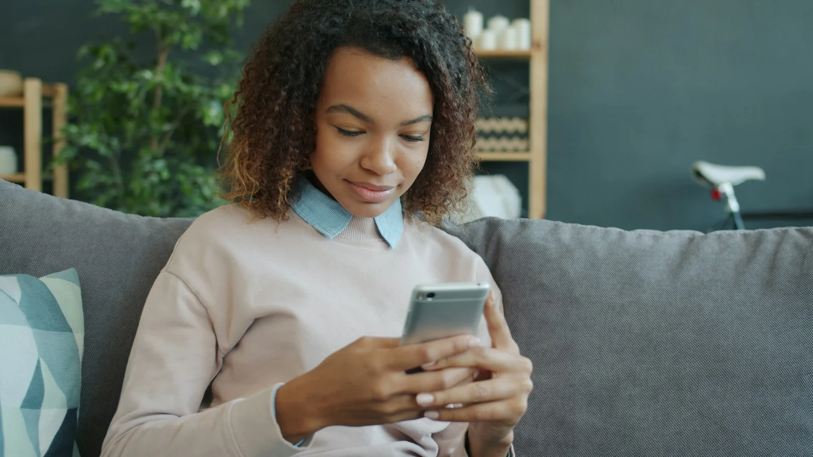 Mulher utilizando um smartphone no sofá, ilustrando a possibilidade de assistir novelas baixadas sem internet