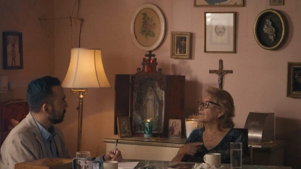 Cena de Poeta Canibal com entrevistador conversando com uma mulher em ambiente doméstico