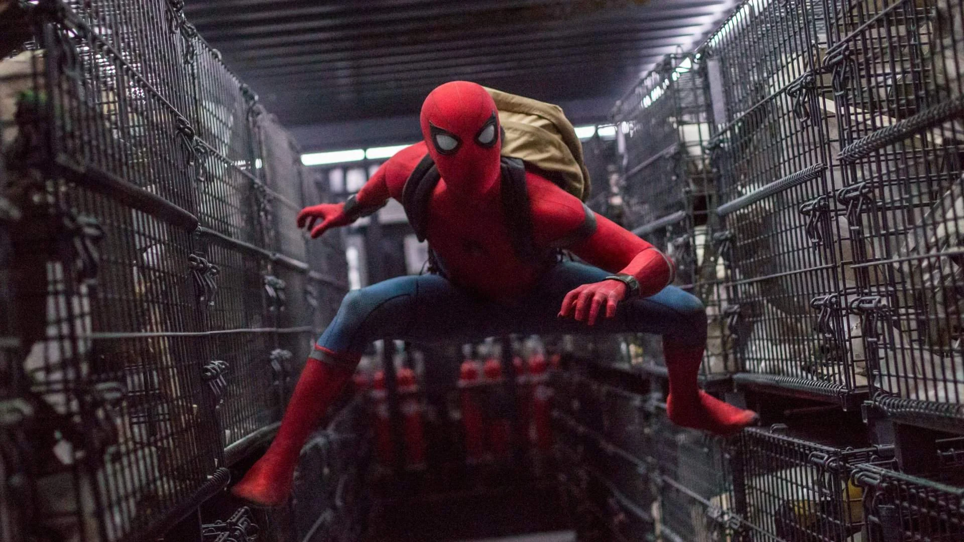 Homem-Aranha, interpretado por Tom Holland, agachado em um corredor de grades metálicas em De Volta ao Lar