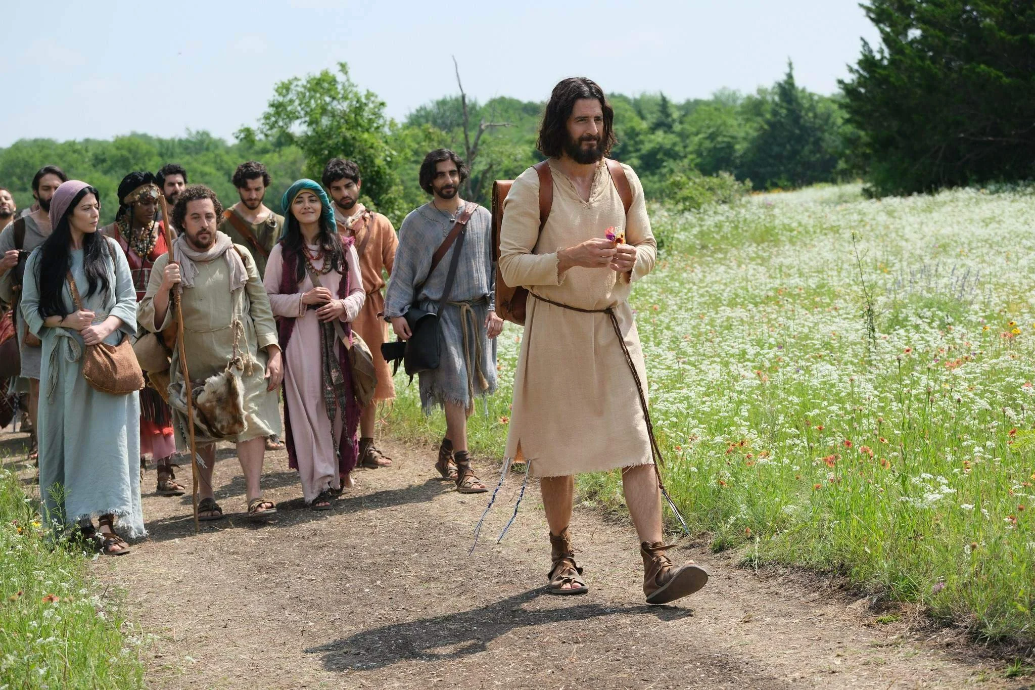 Jesus e seus seguidores percorrem um caminho em meio ao campo em The Chosen