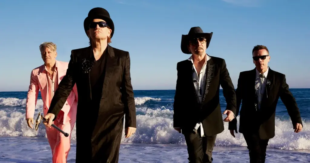 Os quatro integrantes do U2 caminham juntos à beira-mar em fotografia de divulgação do álbum Carnaval De Luz
