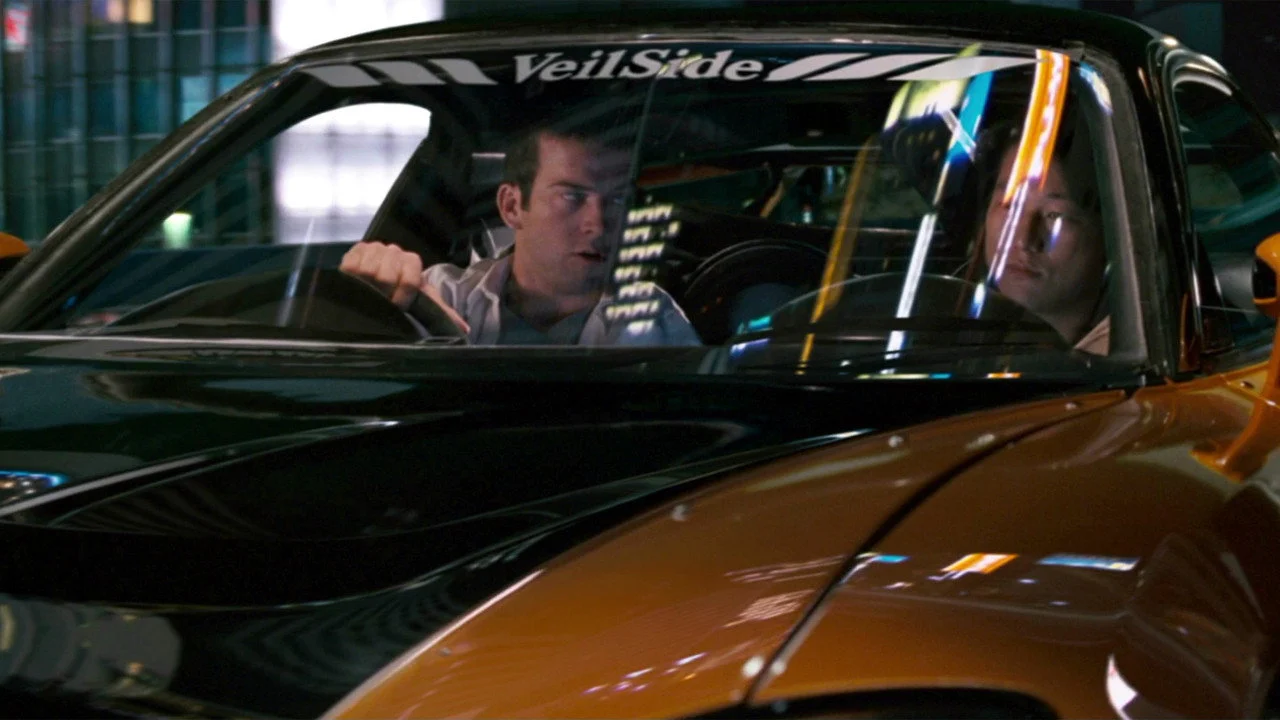 Sean Boswell e Han dentro de carro esportivo preto e laranja em Desafio em Tóquio