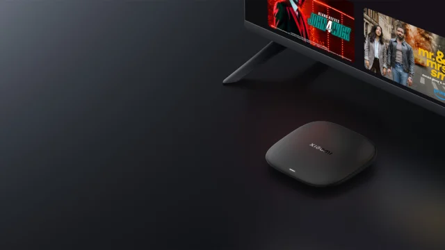Xiaomi TV Box S de terceira geração sobre um móvel, diante de uma televisão